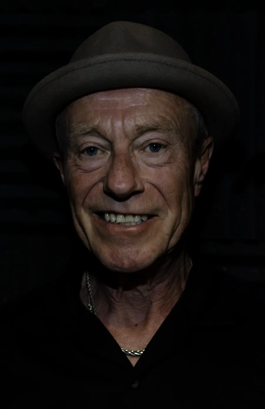 Rich Thair in a brown hat and dark shirt, lit against a black background.