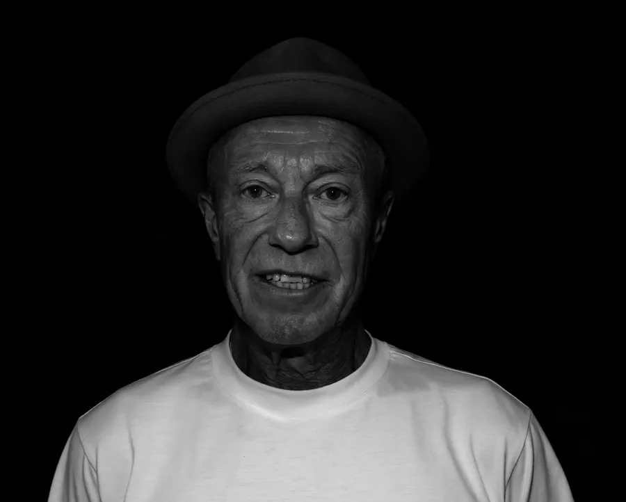 Black and white portrait of Rich Thair in a hat and white t-shirt against black.